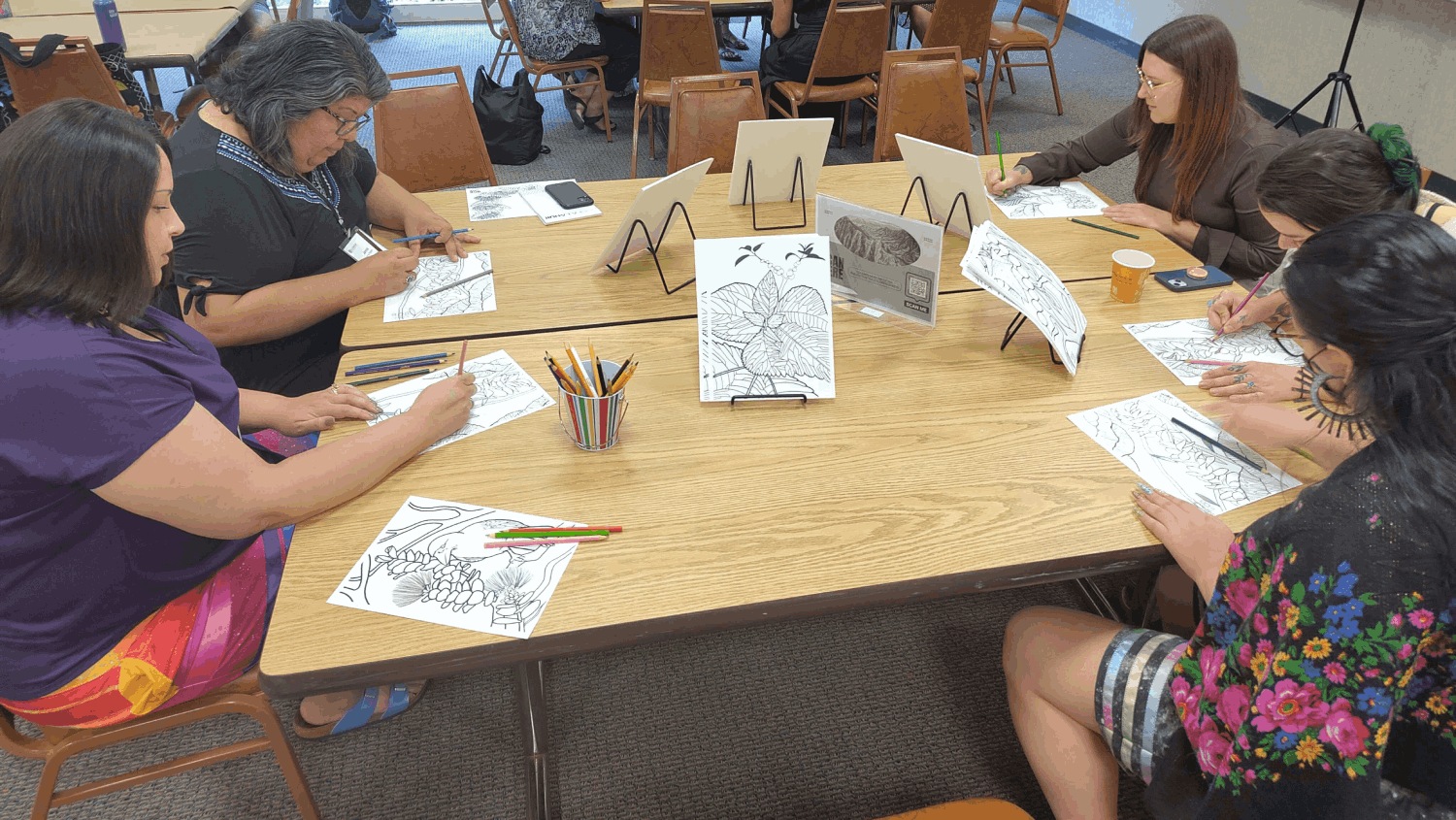 Four forum attendees sit at grouped tables, colouring in Hawaiʻian motif drawings with colour pencils and pens.
