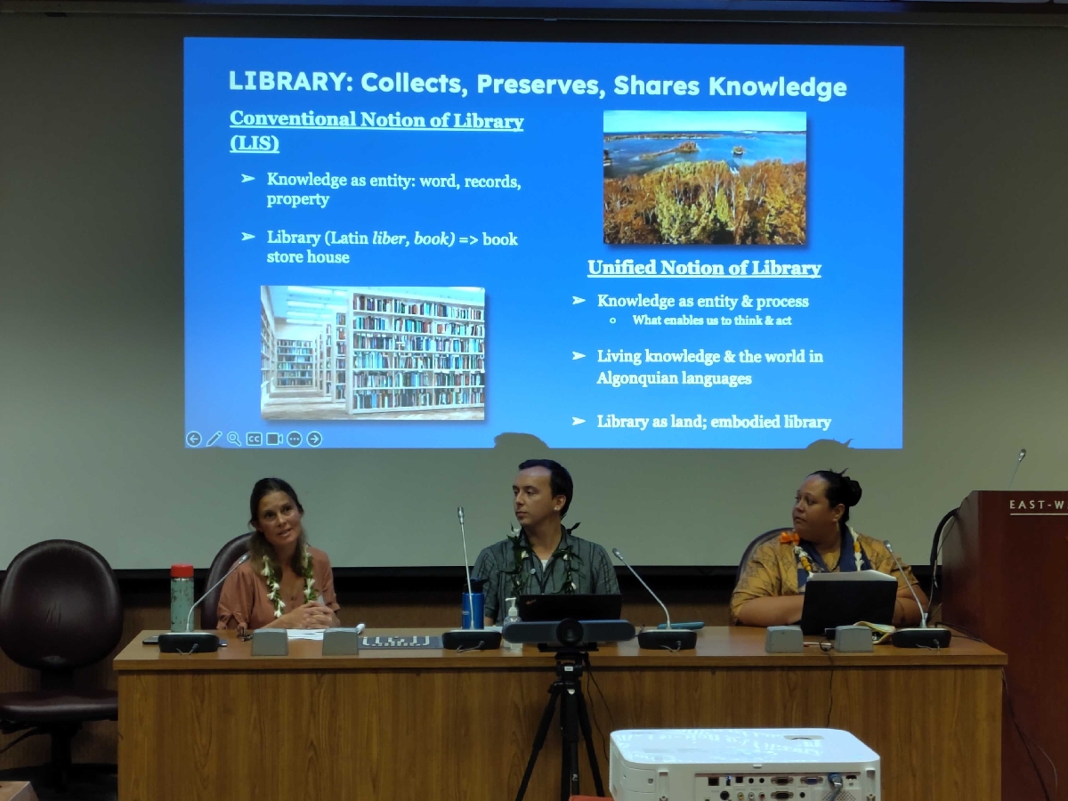 Three seated speakers present a slide titled, "Library: Collects, Preserves and Shares Knowledge" that discusses conventional and unified notions of libraries.