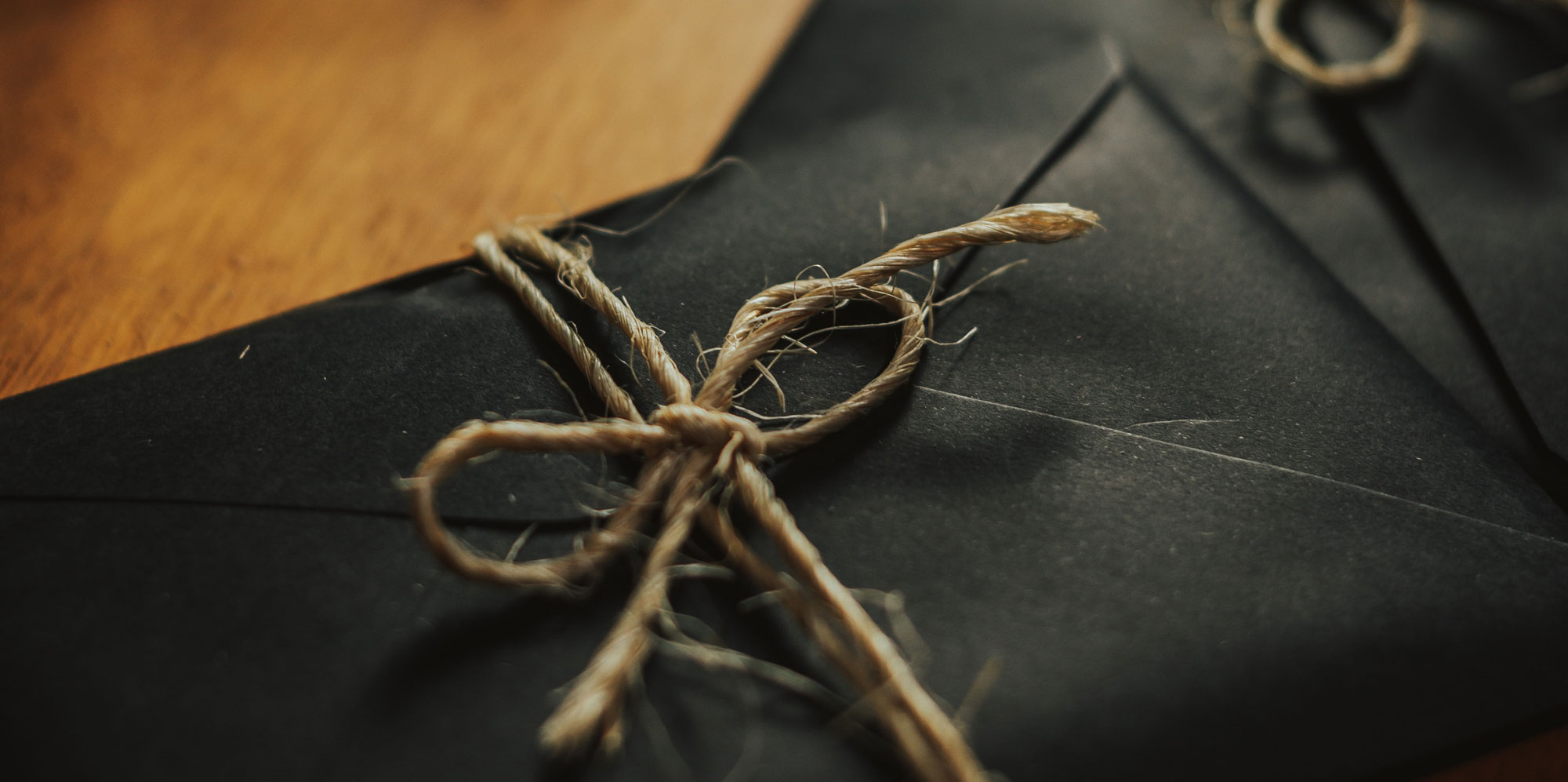 Black envelopes neatly arranged and secured with twine on a polished wooden table.