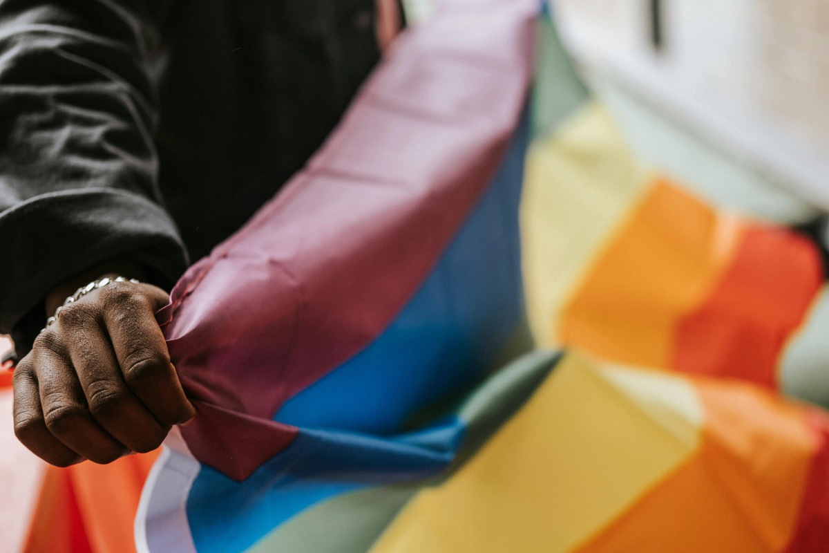 A person holding a rainbow pride flag outdoors.