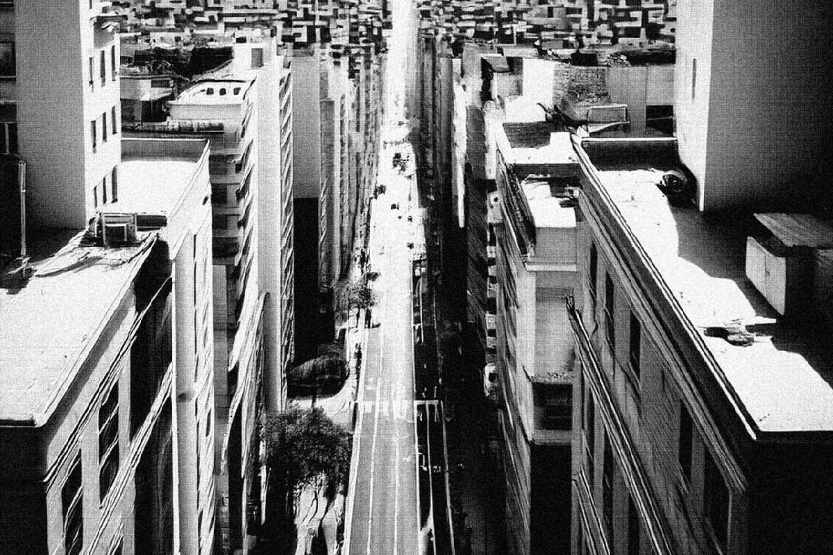 Black-and-white aerial view of a narrow city street flanked by tall buildings.