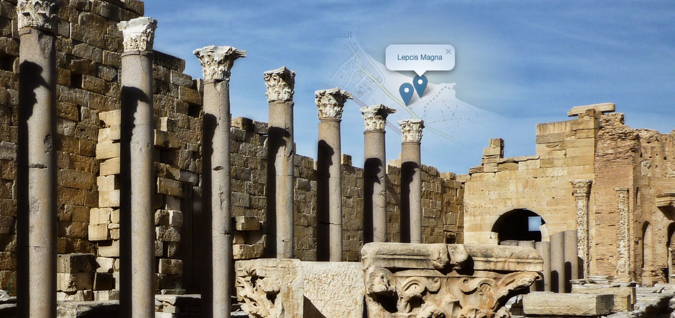 Ancient ruins of arches and building structures with a 'Leptis Magna' location marker overlay with a map