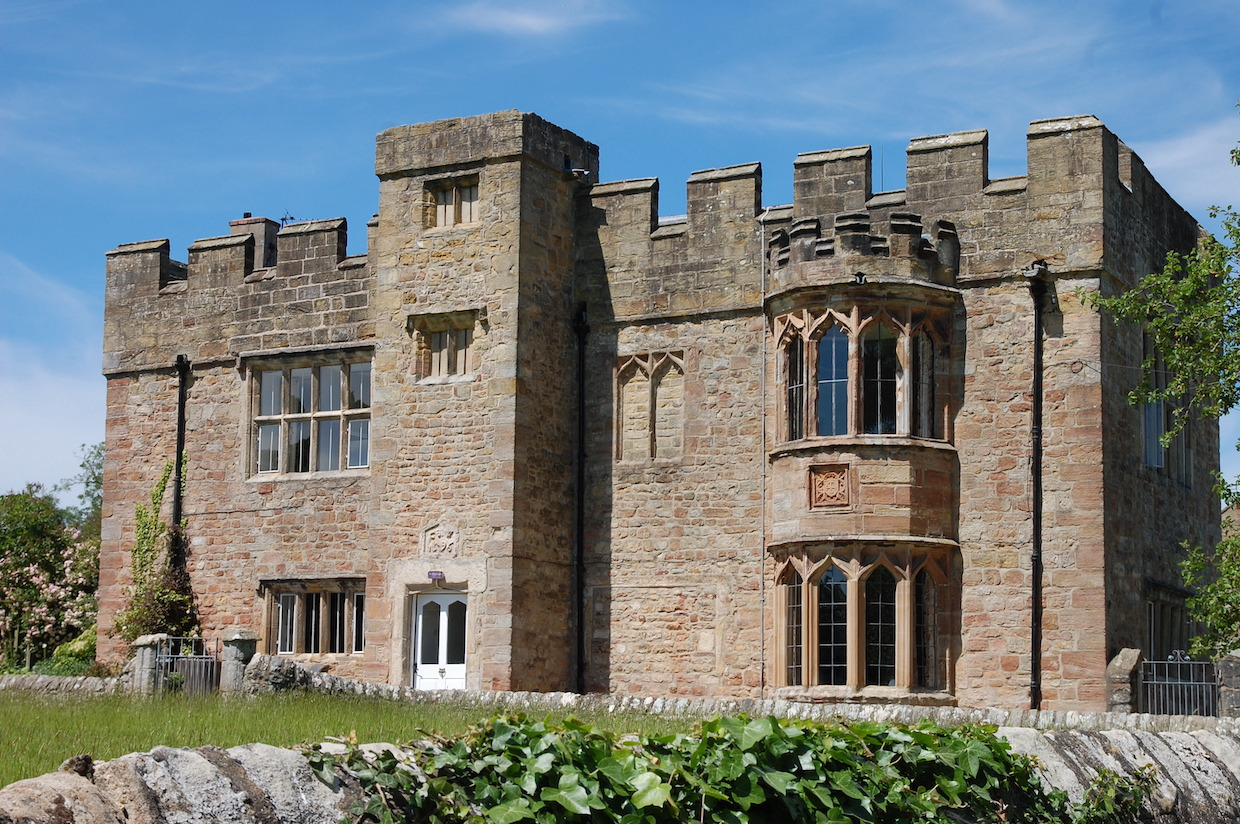 An imposing two storey building made of stone blocks with intricate details set in the countryside.